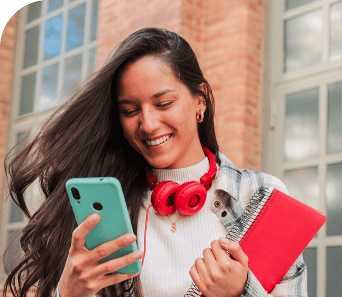A happy young woman holding a red notebook smiles down at her phone